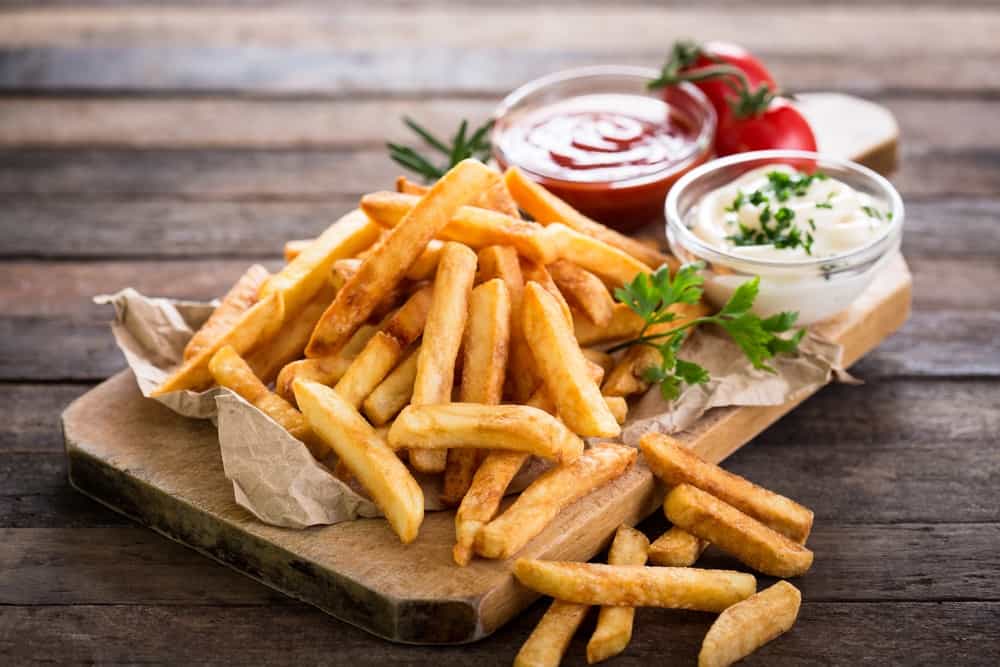 French fries on a wooden chopping board with ketchup and mayonnaise on the side.