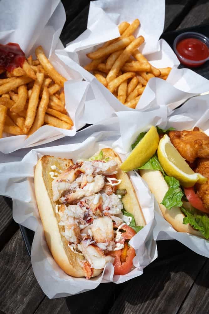 Flat lay of a fresh crab and lobster roll beside golden brown french fries.