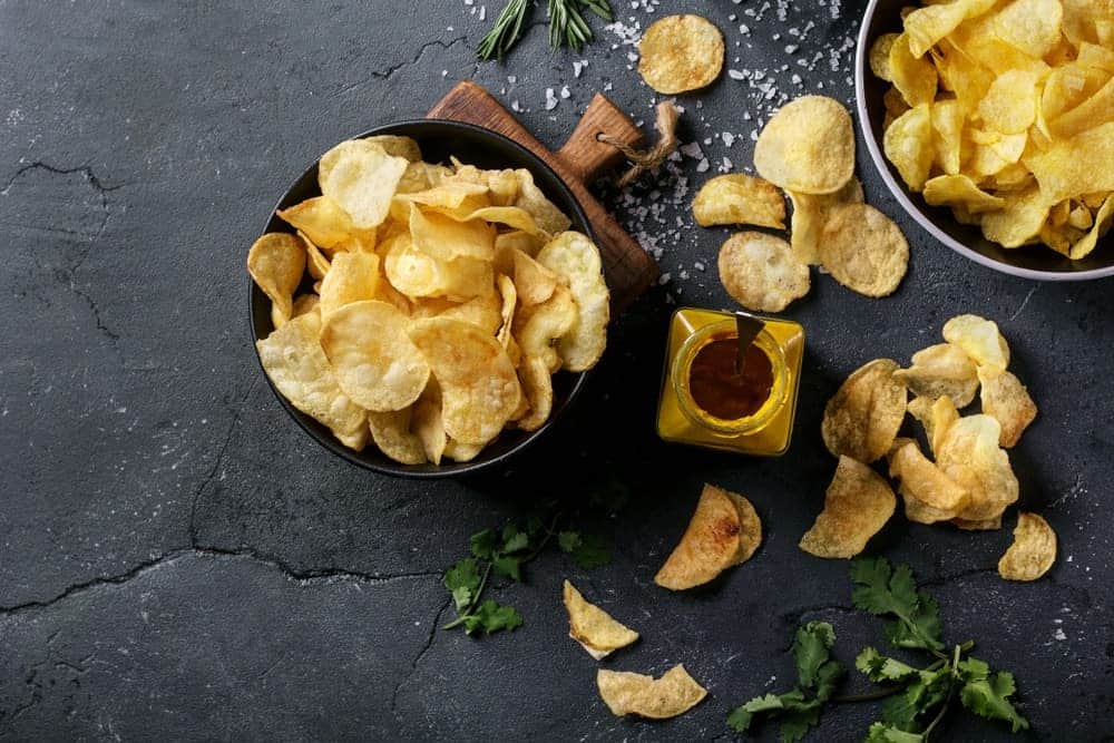 Bowl of home made potato chips served with mustard, rosemary, fleur de sel salt on stone background.