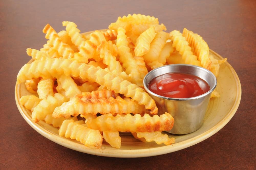 Crinkle cut french fries and a cup of ketchup on a plate.