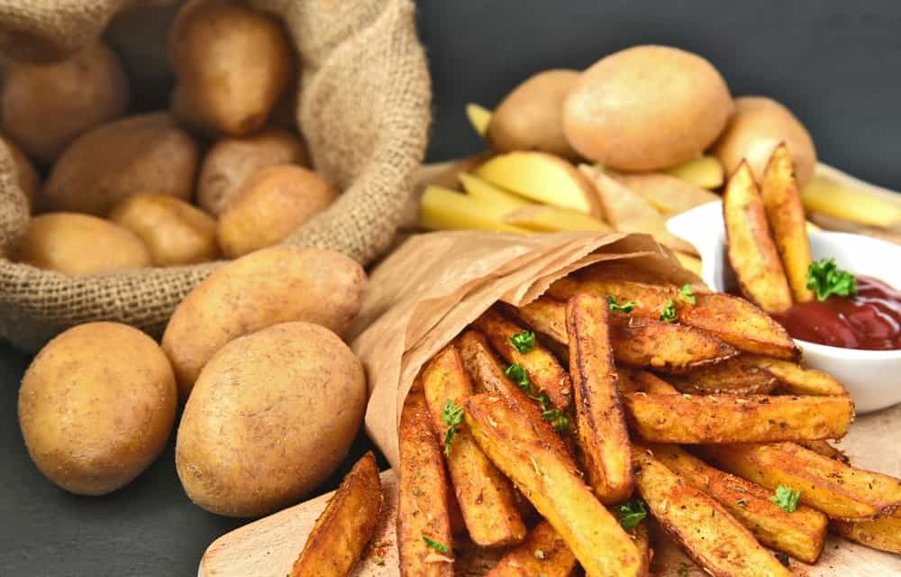 Homemade Crispy Seasoned French Fries. French fries with spicy seasoning in brown paper bag on wooden broad.