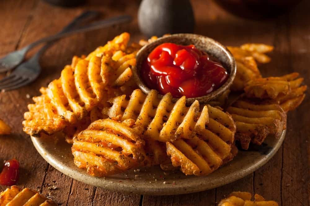 Crispy homemade waffle-cut fries with organic ketchup on a plate.