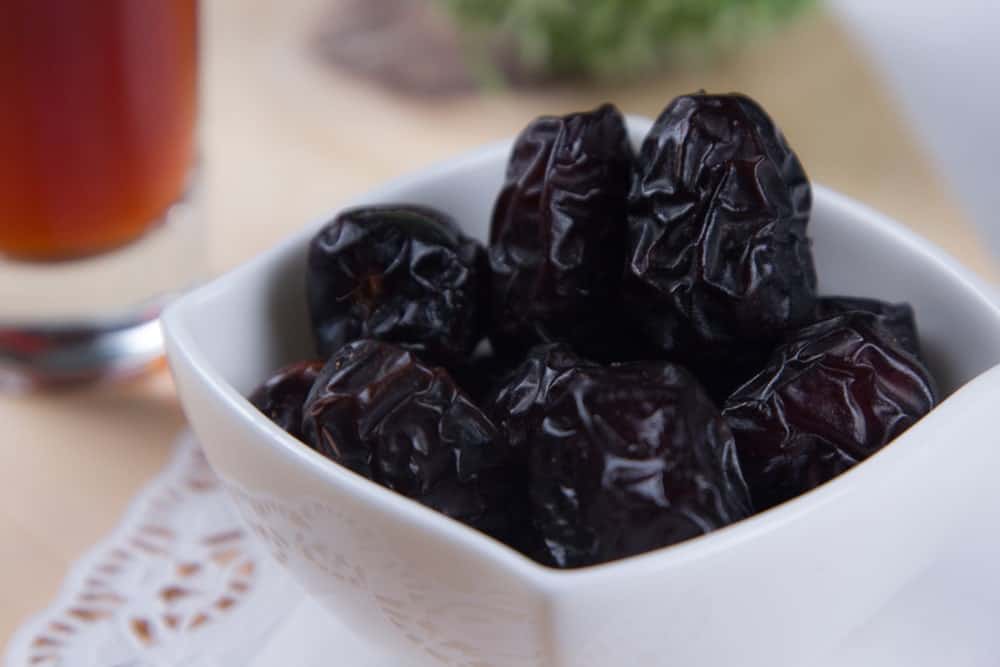 A bowl of Ajwa Dates ready to eat with a glass of sweet tea.