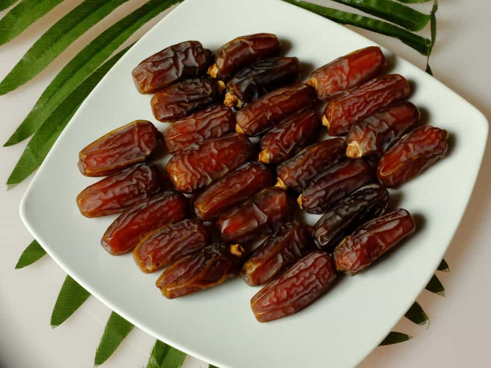 Un plato de deliciosos Dátiles Mabroom sobre un mostrador blanco con hojas de palmera.