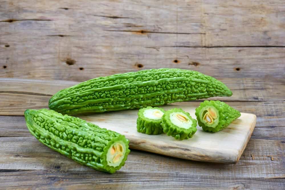 bitter melons with one sliced to show its cottony insides with seeds.