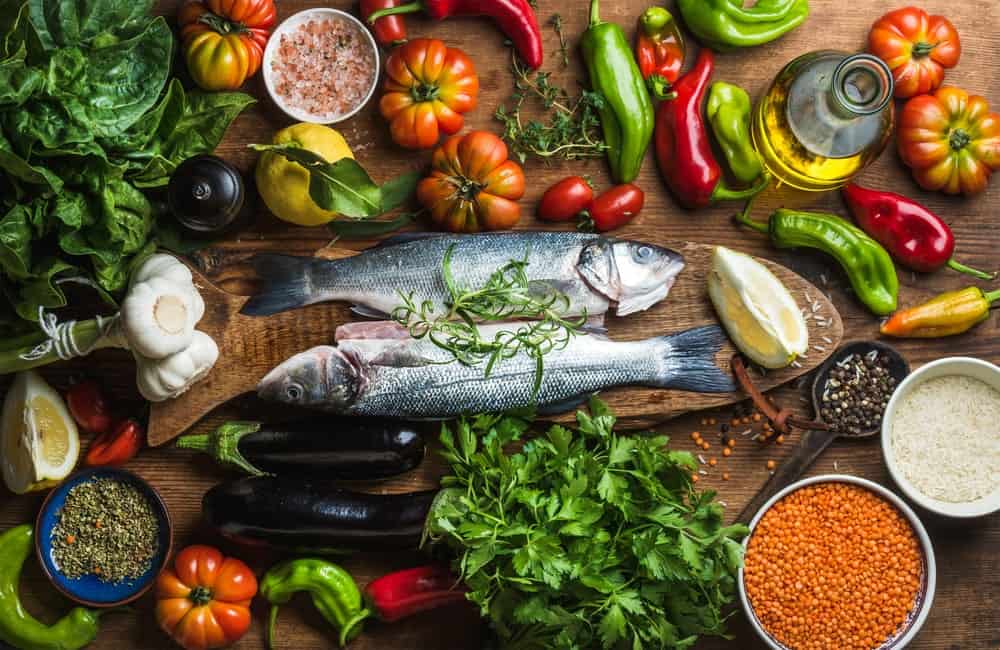 A variety of Mediterranean ingredients surrounding two raw fishes.