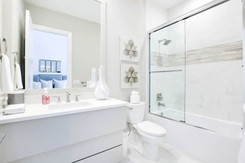 Looking for all-white bathroom designs? This might be the one you're looking for! The dominant color is white, which includes the toilet, the sink counter, and even the shower area, with just a touch of grey tiled ban design for a pop of color. It also has a medium-sized mirror by the sink.