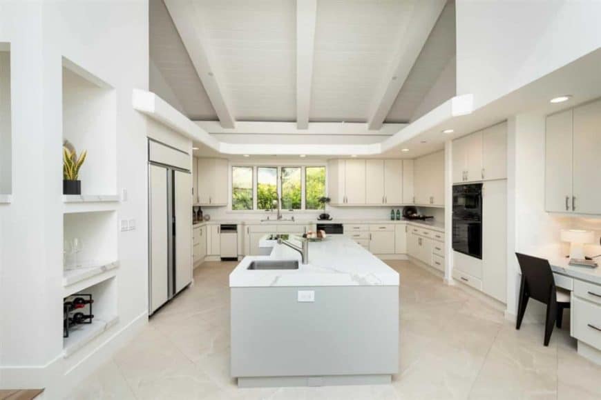This shabby chic kitchen has a nice feminine touch to it with its beige cupboard and tiled flooring, and grey marble kitchen counter. Its white beam ceiling gives it a laidback modern vibe. The black accents add contrast to the light interior of the kitchen.