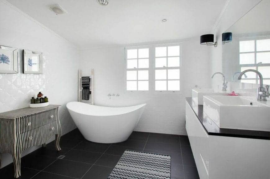 Spacious bathroom with a large oval freestanding bathtub matches the dark marble flooring. Dark wood countertops and flooring compliment the white ceramic bowl styled twin sink basins.