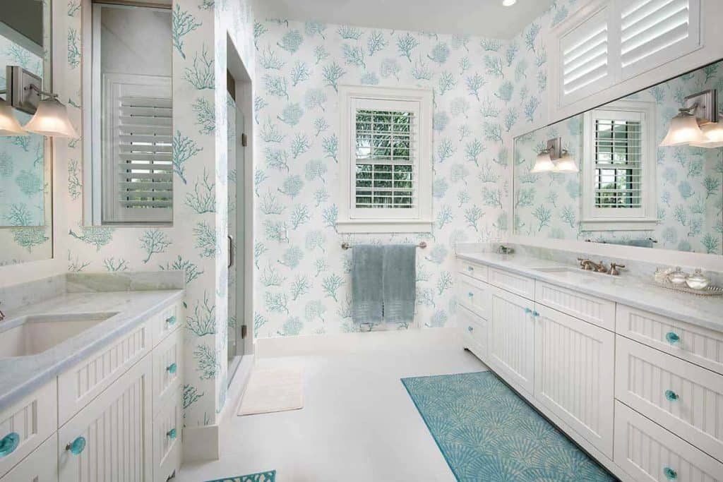 You would adore this beach-inspired bathroom with its white interior with blue accents. The white double-counters have blue handles, the wall art is painted with blue twigs while the blue rug complements the plain white flooring well. The yellow wall lamps provide great lighting for the long mirror installed above the sink.