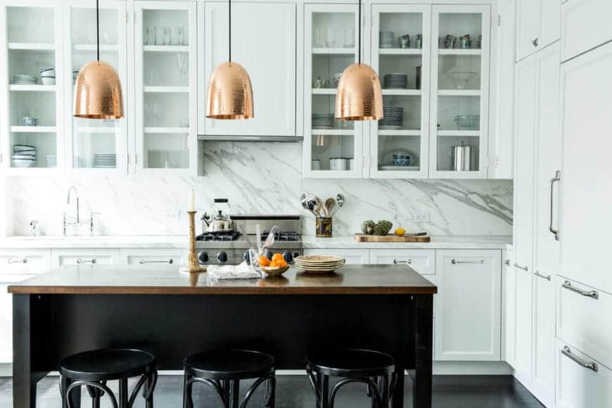 Going for a fancy home kitchen? Take a cue from this design. The marble splashback, white drawers, and dark wood dining bar go great together. For that sophisticated touch, you'll find fine-looking gold pendant lightings directly above the dining table, to light up the entire kitchen.