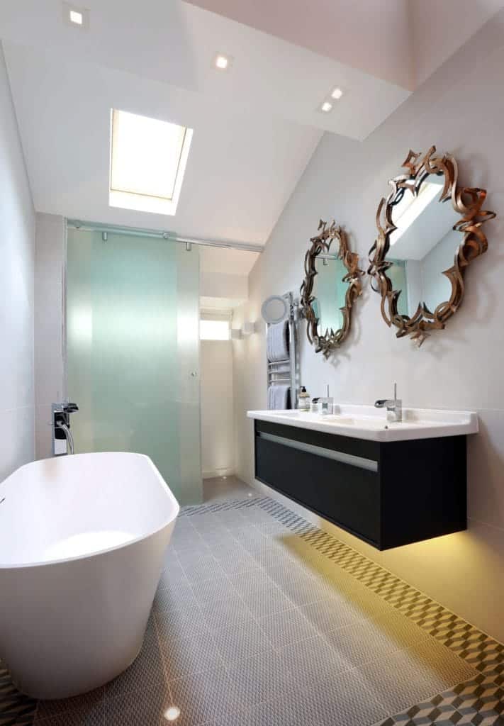 The modesty of the pure white walls and standard sized off white tiles complement the modern elements of the wall and white vaulted ceiling. This bathroom has stylish mirrors under the sink basin.