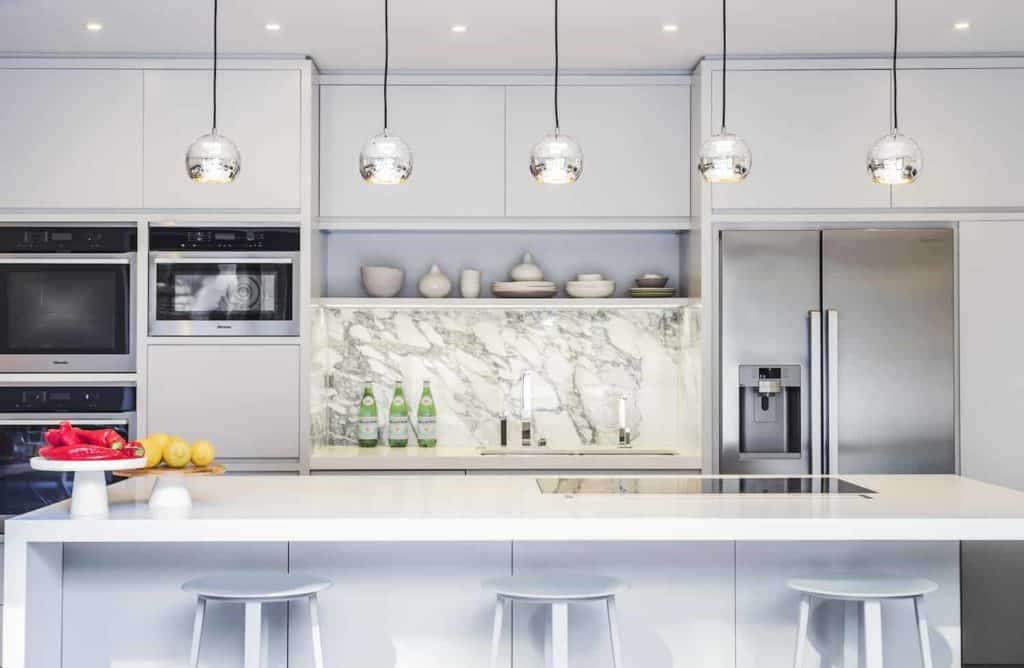 This kitchen features a steel 2-door fridge, sink with marble backsplash, and generous pantries for all your go-to ingredients. It has a disco pendant lighting over the long white island with also the white bar stools for convenient eating.