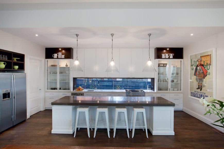 If you're looking to build a contemporary kitchen, you might want to take this kitchen for inspiration. It features a single island with a white bar and smooth brown countertop, with a translucent inverted triangle pendant lightings. These go well with the hardwood flooring. The drawers and shelves are also painted white for a fresh and modern look. Recessed lightings are also present on the ceiling.