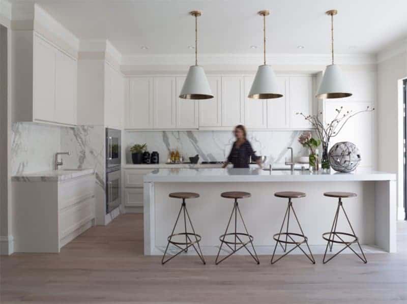 How about a Scandinavian inspired kitchen? This kitchen has a white island with built-in sink, marble splashback for a touch of color, and beautiful pendant lighting with gold tubing and canopies. The uniquely shaped bronze bar stools also go well with the dusty rose-coloured flooring.