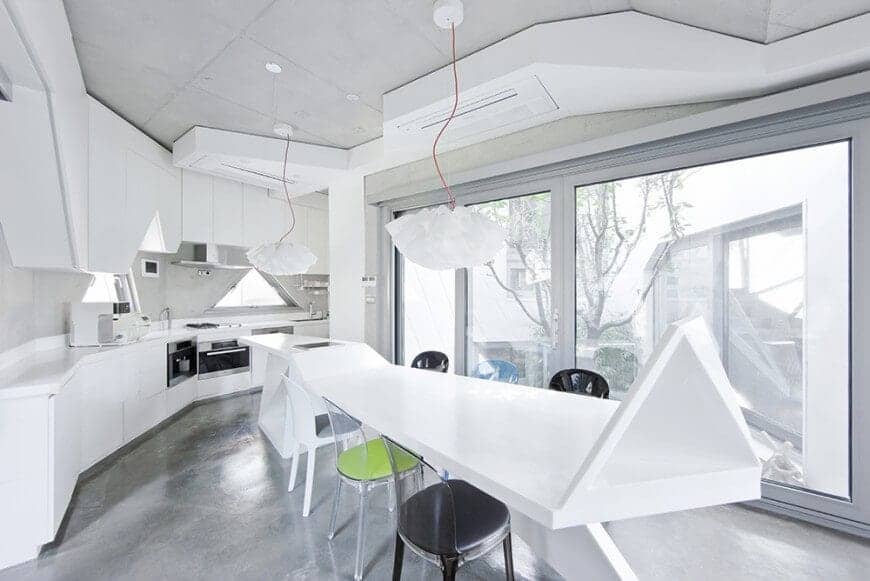 This kitchen has an eclectic design that goes perfectly if you like geometric shapes, like this white dining table with different colored chairs, with floral-shaped pendant lights above. It gives the entire room a bright look especially with the white counter with the appliances right under.