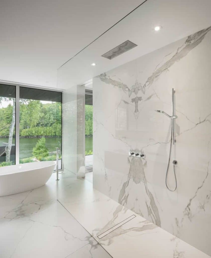 For a minimalist and functional design, you'll love this bathroom with its walk-in shower while sharing the open space with a freestanding tub. The marble flooring and walls, plus the recessed lights, give it a nice fancy touch without making it look over-the-top. The floor-to-ceiling glass window provides a refreshing view of the outdoors.