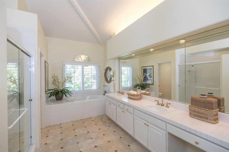 This white bathroom featuring white walls and a white ceiling. This room also has a large mirror and a wooden cabinet under the basin sink.