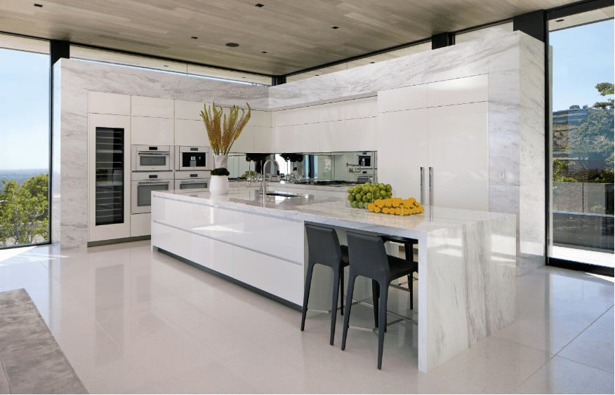 This open kitchen has a marble design both on the countertop and the pantry side panels, which perfectly complement the kitchen's entire white interior. This is also laden with a long island in the middle, with two black bar stools for comfortable seating. With the tan faux wood ceiling in place, you can be sure this suits the floor-to-ceiling glass windows for that polished finish.