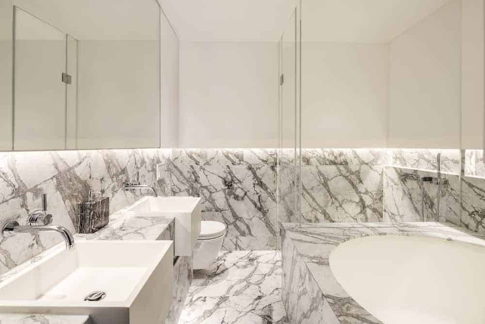 The white primary bathroom has a white double sink match with contemporary countertops and elongated bathtub.