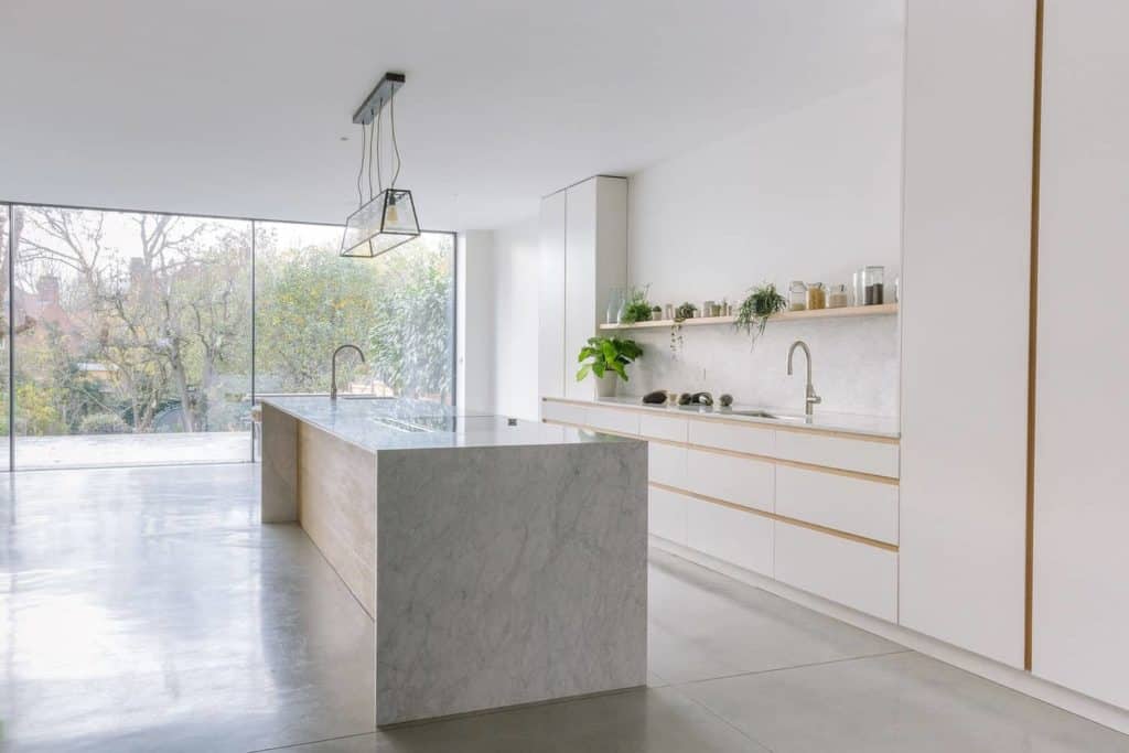 White and marble go well together especially if you're going for a simplistic urban kitchen design. The marble countertop complements the white walls with beige linings, the indoor plants on the upper shelf also make the kitchen look livelier, while the floor-to-ceiling glass windows and the translucent pendant light make a nice touch for the overall design of the kitchen.
