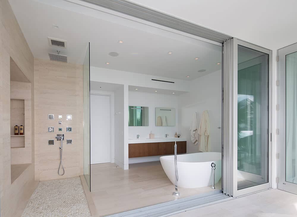 A white and brown style wall mounted waterfall shower head combines with the handheld showerhead and glass paneling to make this the ultimate place to freshen up. It also has vintage-looking bathtub.