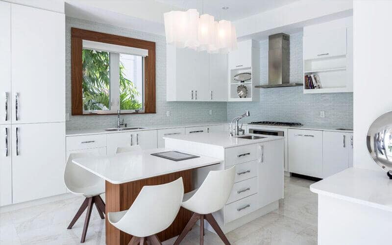 For a modern take, this kitchen has a combination of white, wood, and blue aesthetics. You got white drawers, shelves, kitchen bar with sink, and dining tabletop and chairs, while the walls have a dainty blue pattern. With wooden accents, a glass window, and white rectangular pedestal lights, this kitchen looks good for any tiny space.