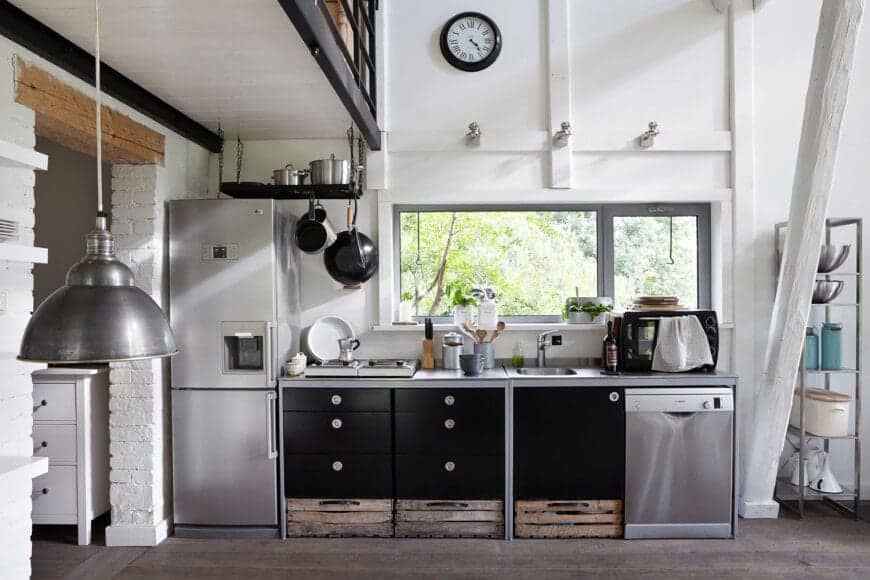 This kitchen showcases the perfect combination of rustic and industrial with its steel appliances and matte black drawers. The wooden crates and hard flooring add texture to the whole kitchen, while the white walls and panels add a nice contrast for a soft touch.