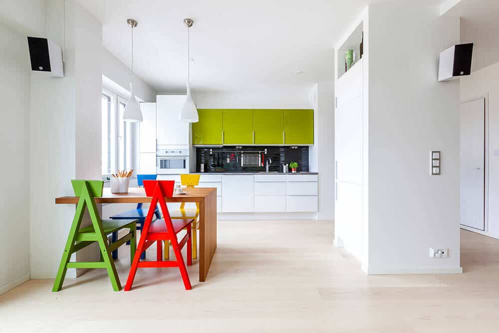 This chic kitchen has a playful touch to it with its colorful dining set and bright green cupboard, which is a good contrast to the white drawers, pendant lights, and the large pantry in the middle of the kitchen.