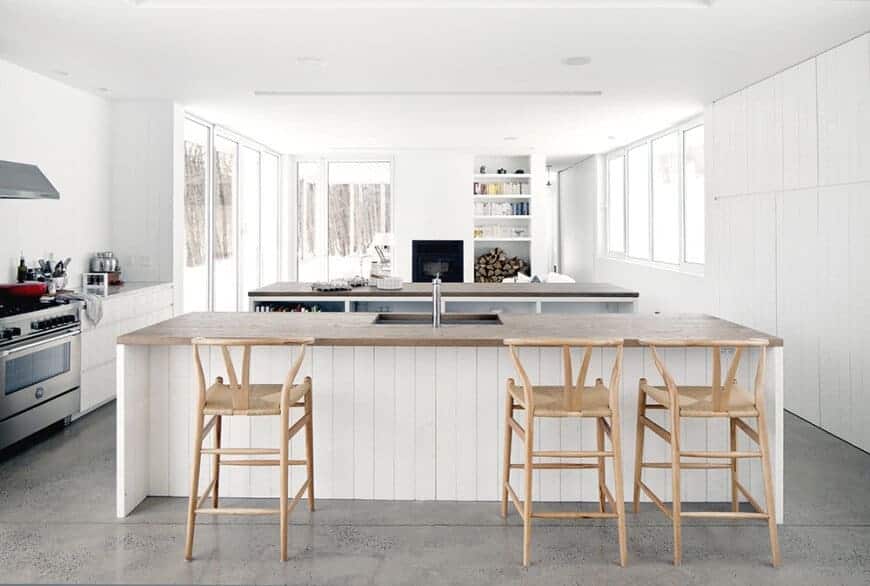 This Scandinavian inspired kitchen has a lovely combination of white double islands with matte wood countertops. The double peninsula provides plenty of room for kitchen utensils and cookware. The light-colored wood stools also look great for the entire room. With the grainy grey flooring, this gives just the right amount of contrast to the light interior of the kitchen. Finish it off with floor-to-ceiling glass doors, and windows, and you got a nice Scandinavian kitchen.