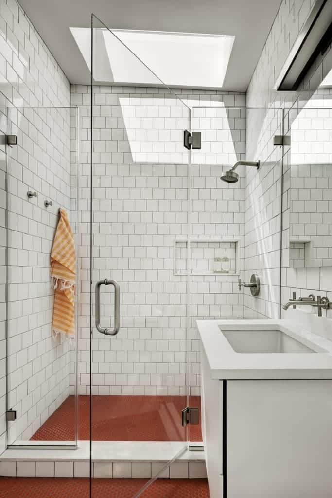 This primary bathroom boasts a walk-in shower and a floating light wood vanity fitted with sink and chrome pulls. It also has a high vaulted ceiling.
