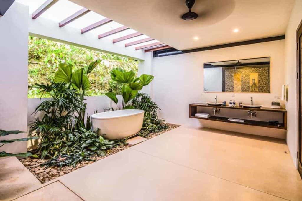 Large primary bathroom featuring freestanding bathtub and plants. This room also has wooden countertops with dual sink.