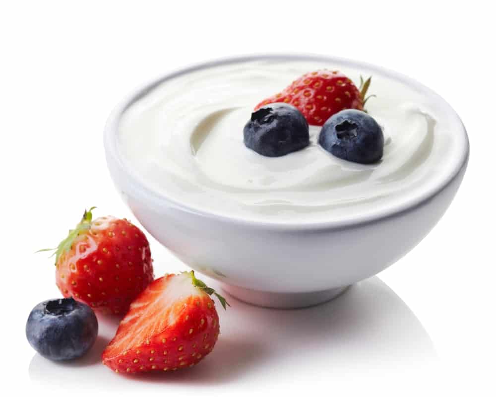 A bowl of yogurt with strawberry and blueberries.