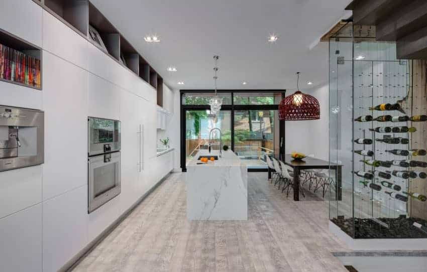 Put a twist in any urban kitchen with an attractive pendant light like the red woven lighting in this kitchen. The recessed lights also help liven up the room. The kitchen has a marble island with sink in the middle of the room, with a ready long dining table just in front of it. To finish, it has a nice combination of wooden flooring and white kitchen drawer.
