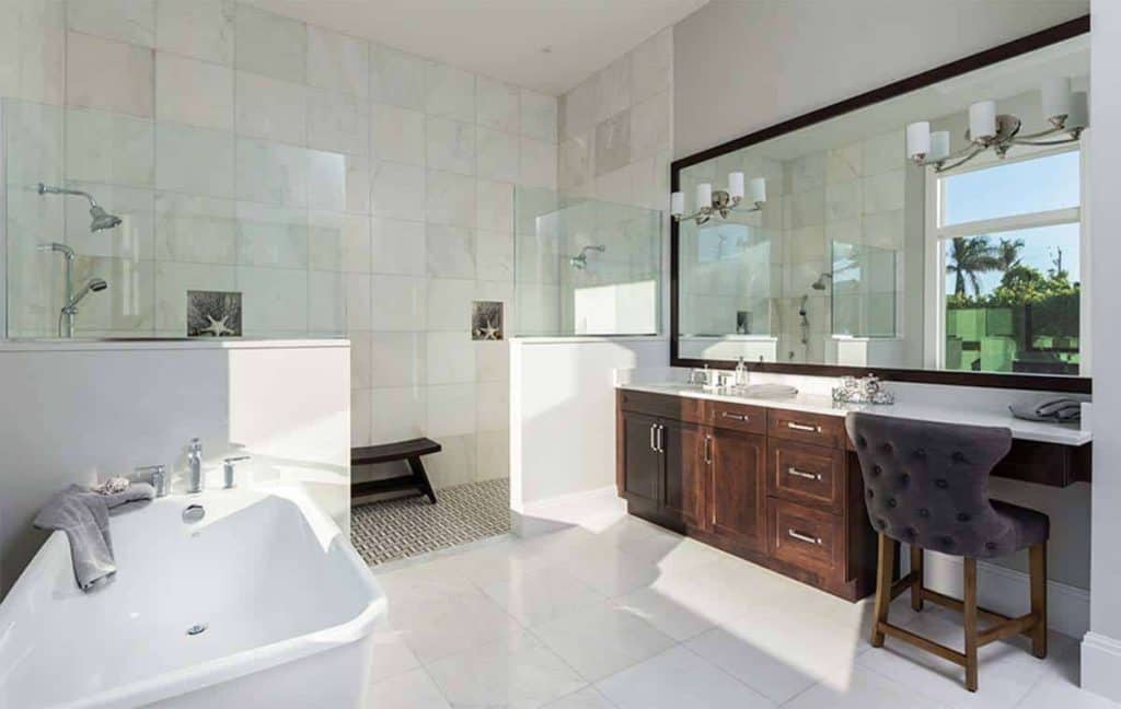 For a more contemporary take, this bathroom shows a mix of white and brown with the white tile flooring and the bathtub while you would immediately notice the brown accent on the vanity drawer which also comes ready with a cushioned chair. The mirror's frame also matches the brown accents of the bathroom. With a walk-in shower area with a resting chair and a bathtub in the open space, you can be sure this bathroom is versatile on its own.