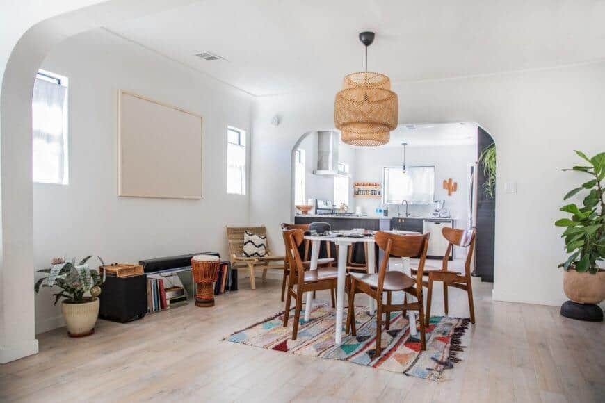 A dine-in kitchen featuring hardwood flooring and a small round table with wooden chairs on the rug. This room also has a white wall and a white ceiling with gorgeous hanging lights.