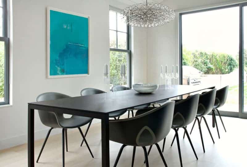 Full view of dark wooden tables with modern chairs brightens up by stunning chandelier. This room has a glass sliding door leading to the garden.