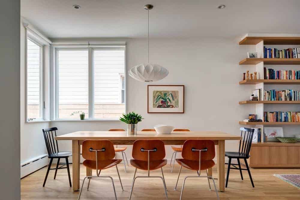 Full view of the wooden dining tables and chairs lighten up by pendant light. This room features hardwood flooring and a glass window.