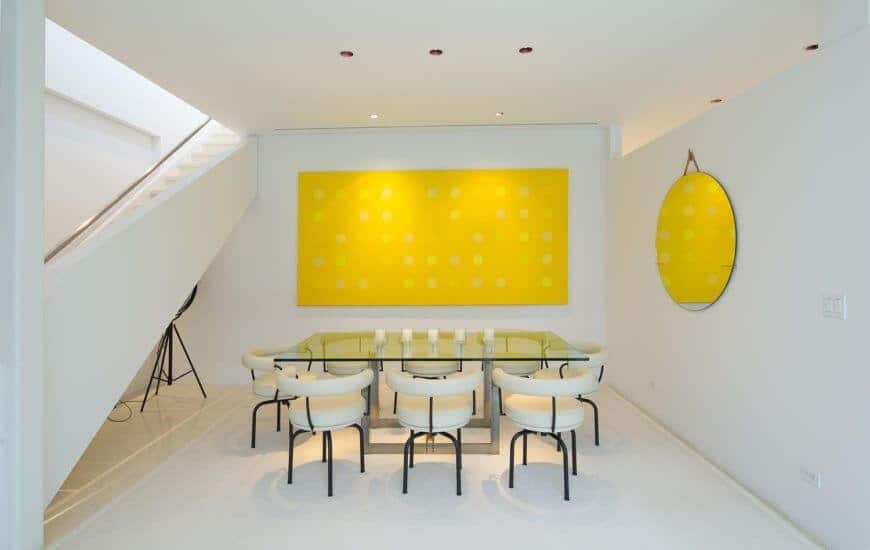 White modern dining room featuring glass tables and stylish chairs. It also features white walls and huge wall decor.