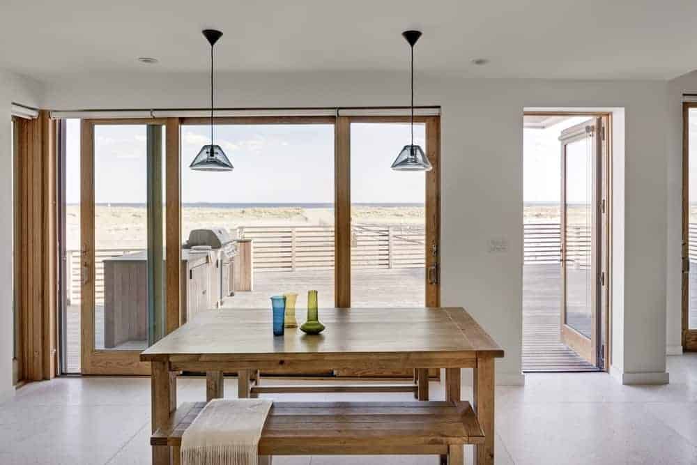 mall dining area with wooden table set with a pair of wooden bench and brighten by pendant lighting. This room also has a large window and glass door leading to the balcony.