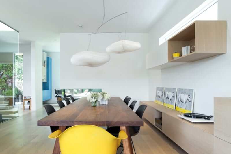 White dining area featuring wooden tables with pairs of black chairs lighted by the chandelier. This room also features white walls with wall decors.