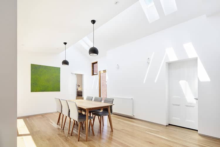 White dining area featuring white walls and a white ceiling. Wooden table and grey chairs brighten by hanging ceiling lights.