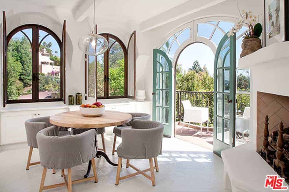 A small dining area with round wooden tables mixed with grey wooden chairs in front of large glass entryway leading to a small balcony. This room features a large window with a beautiful ambiance outside.