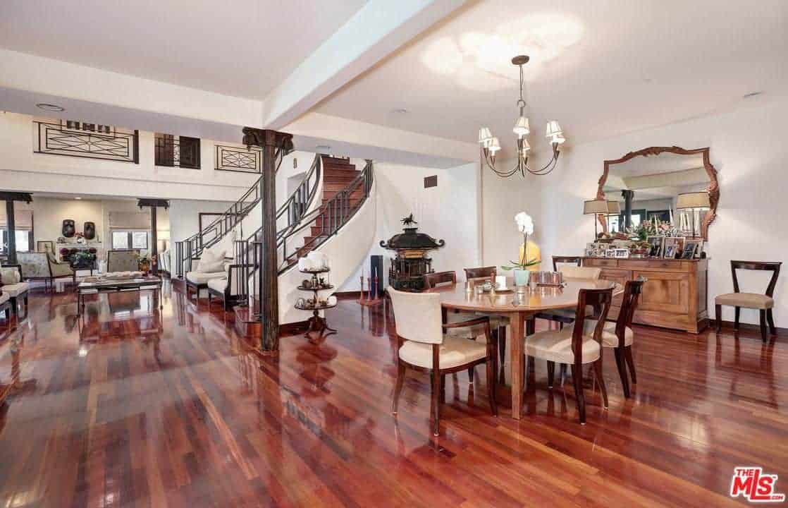 Large living space and dining area with gorgeous hardwood flooring and white walls. The round small wooden table paired with brown chairs lighted by the chandelier.