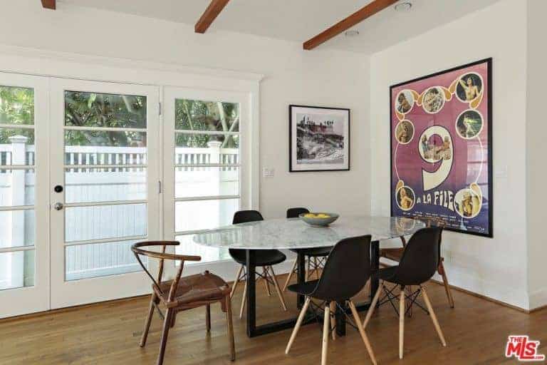 Small dining area featuring a glass oval table with modern chairs on stylish hardwood flooring. This area has a white ceiling with huge wall decors and a doorway leading to the terrace.