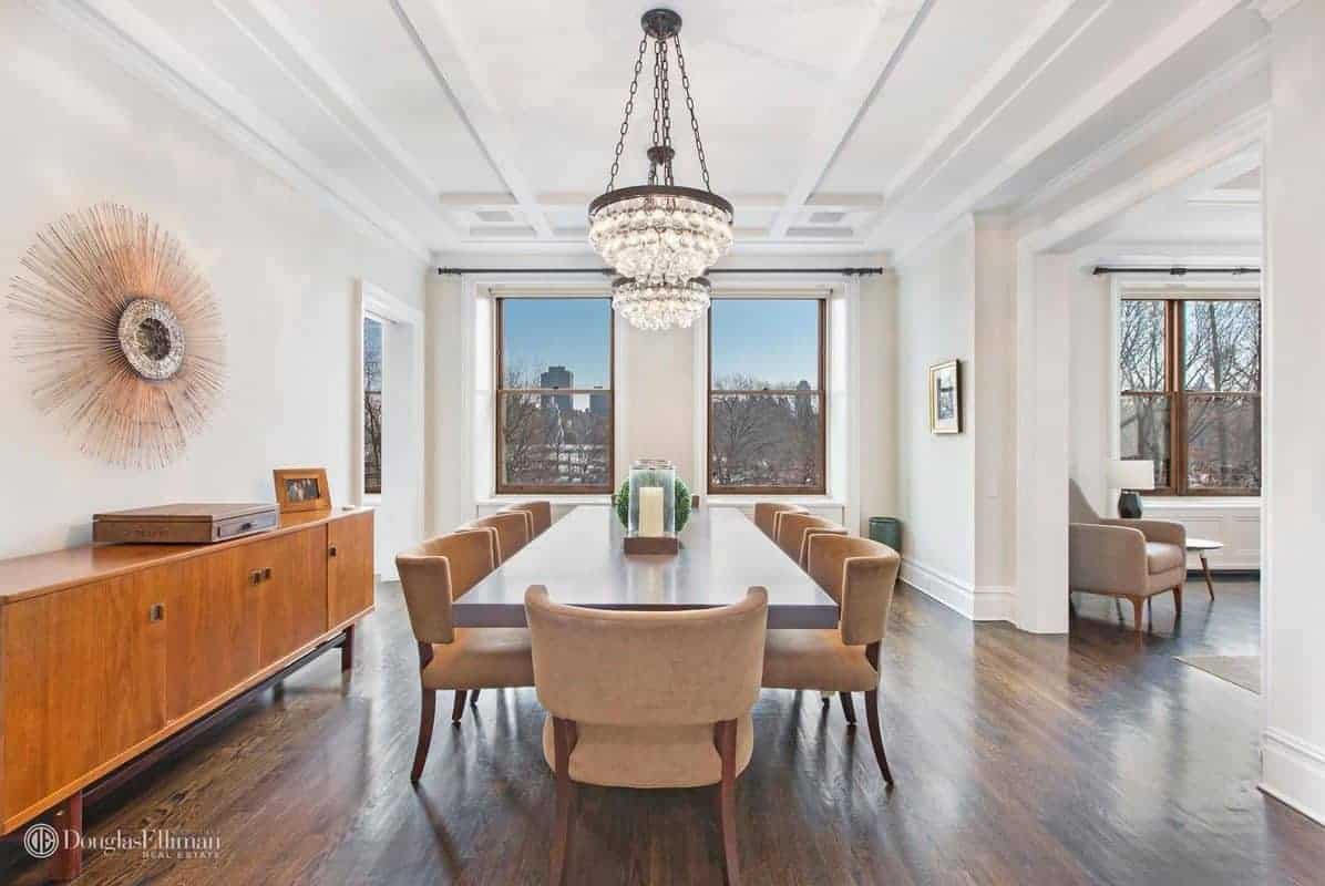 A modern room featuring a living space and a modern table paired with brown chairs on hardwood flooring lighted by a stunning chandelier.