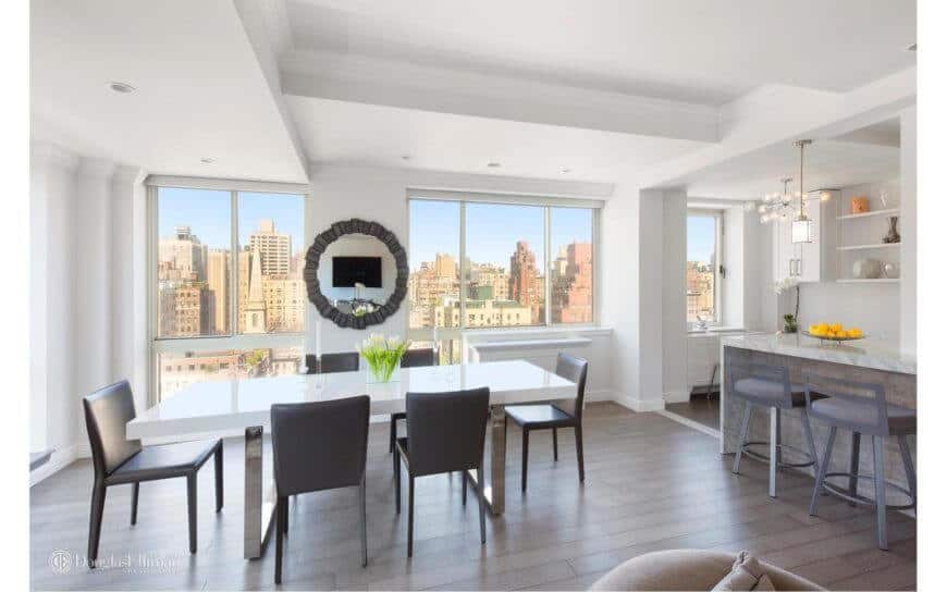 White dining area featuring hardwood flooring and elegant table set with black chair. This room also features a white wall and a large window with a building view outside.
