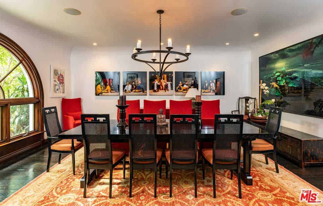 Full view of dining area featuring dark wooden tables and chairs on the rug. This room also features a white wall with multiple wall decor lighted by the gorgeous chandeliers.