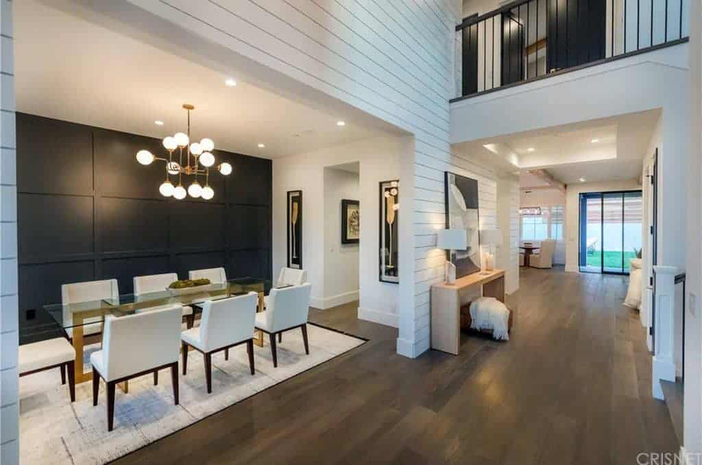 A modern room features a dining area and a living space. Glass rectangular tables pairs with white chairs on the rug lighted by a stunning chandelier.