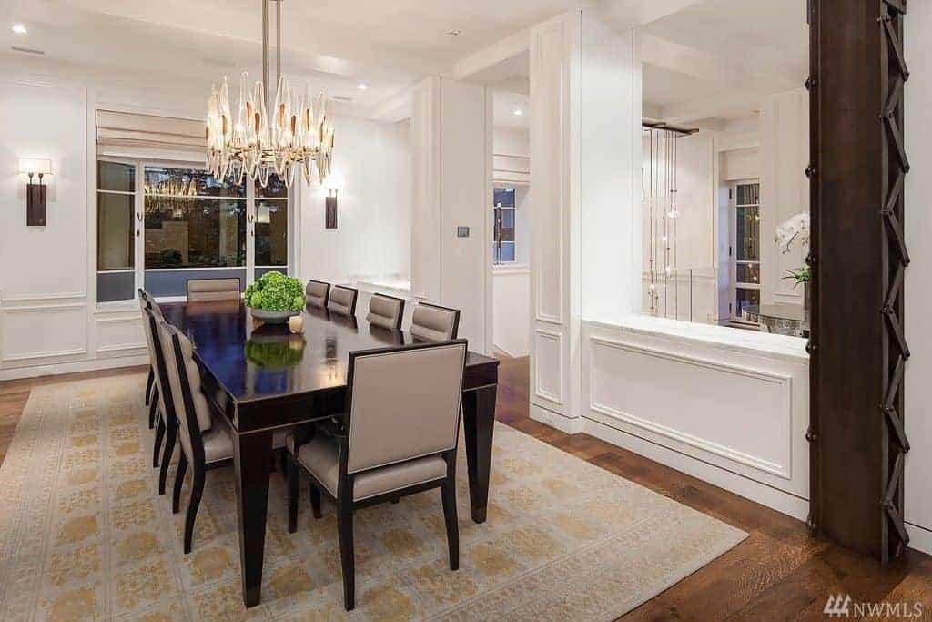 This contemporary dining room featuring a black dining table matched with gray seats lighted by an impressive chandelier.